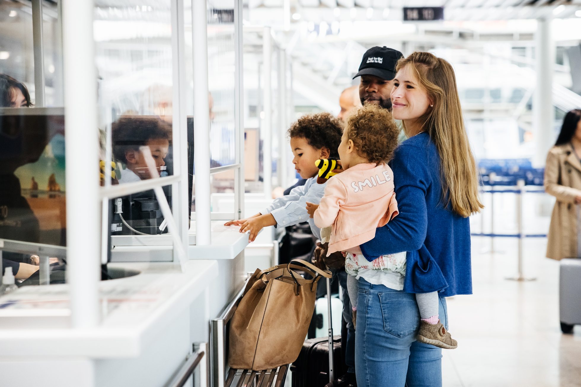 A happy family with two children checks in at an airport counter, smiling and ready for their journey.